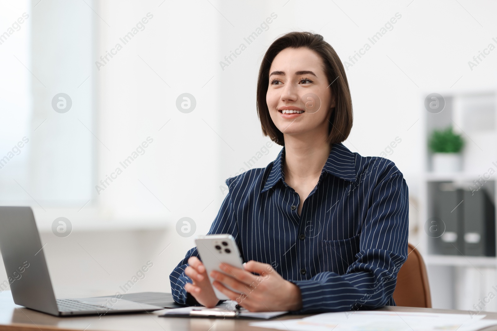 Beautiful woman using her smartphone while working at desk in office. Space for text Photo of Beautiful woman using her smartphone while working at desk in office. Space for text