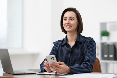 Photo of Beautiful woman using her smartphone while working at desk in office. Space for text