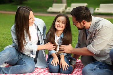 Photo of Happy family sitting on checkered picnic blanket outdoors
