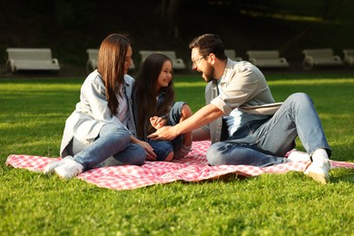 Photo of Happy family sitting on checkered picnic blanket outdoors