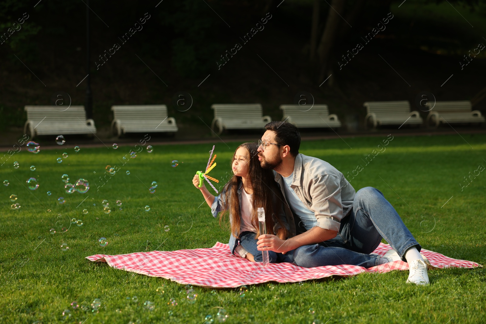 Family getaway. Father and daughter blowing soap bubbles on checkered picnic blanket outdoors Photo of Family getaway. Father and daughter blowing soap bubbles on checkered picnic blanket outdoors