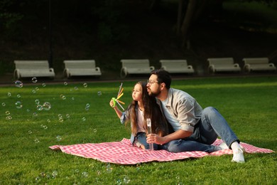 Photo of Family getaway. Father and daughter blowing soap bubbles on checkered picnic blanket outdoors