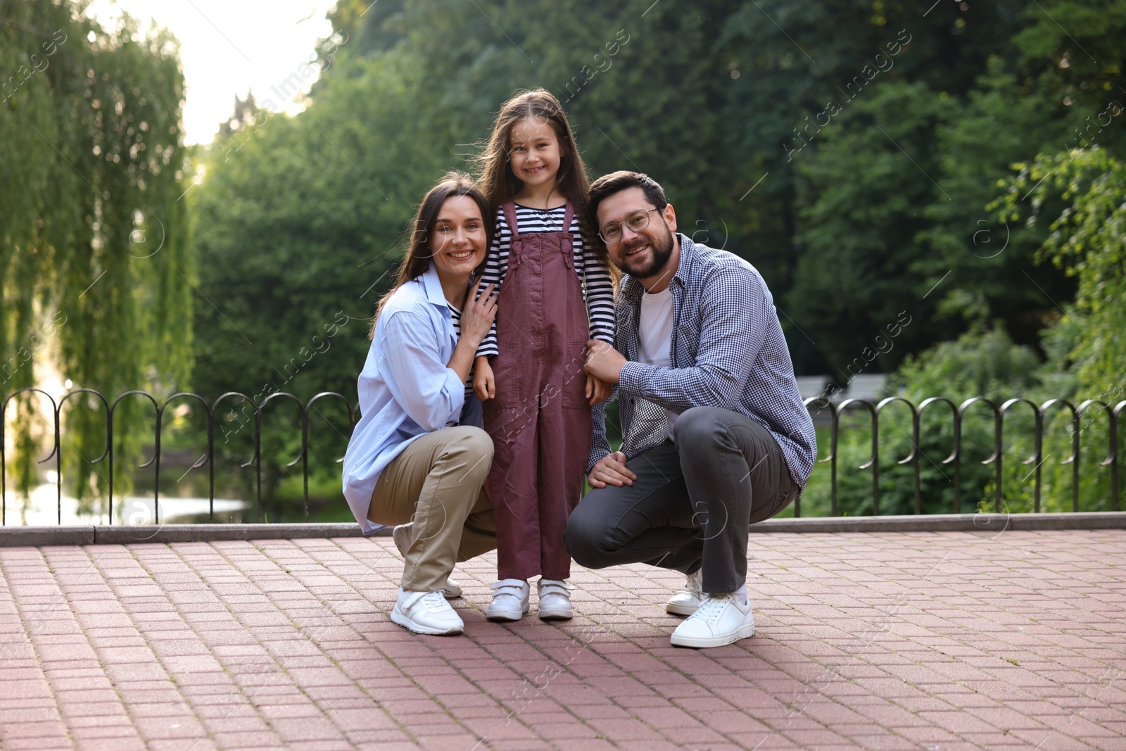 Family weekend. Smiling parents and daughter posing in park Photo of Family weekend. Smiling parents and daughter posing in park