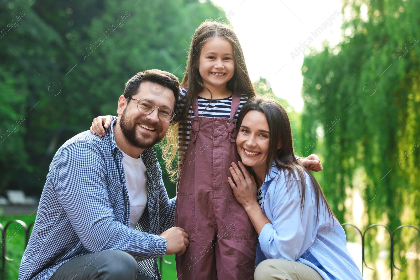 Photo of Family portrait of smiling parents and daughter in park
