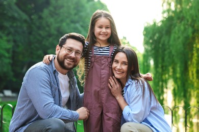 Photo of Family portrait of smiling parents and daughter in park