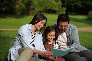 Photo of Family getaway. Happy parents and daughter reading book in park