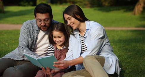 Photo of Family getaway. Happy parents and daughter reading book in park
