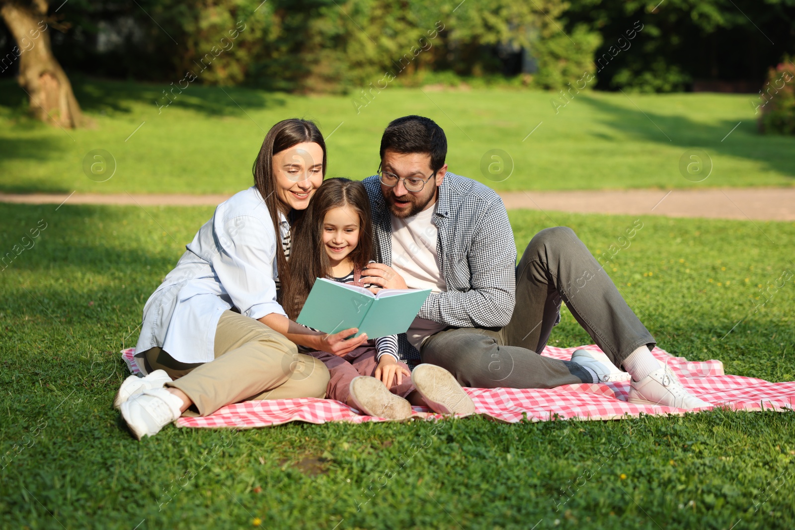 Family getaway. Happy parents and daughter reading book in park Photo of Family getaway. Happy parents and daughter reading book in park