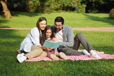 Photo of Family getaway. Happy parents and daughter reading book in park