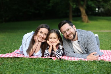 Photo of Happy family posing on checkered picnic blanket outdoors