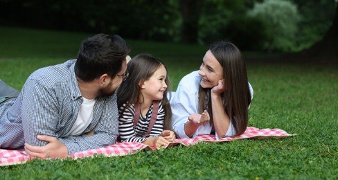 Photo of Happy family spending time together on checkered picnic blanket outdoors