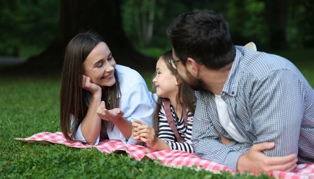 Photo of Happy family spending time together on checkered picnic blanket outdoors
