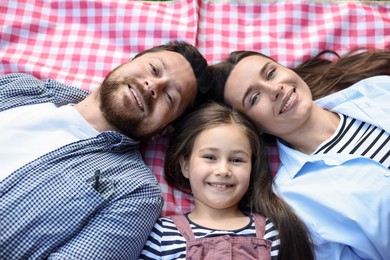 Photo of Family portrait of happy parents and their daughter on checkered picnic blanket outdoors, above view