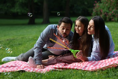 Photo of Happy family blowing soap bubbles on checkered picnic blanket in park