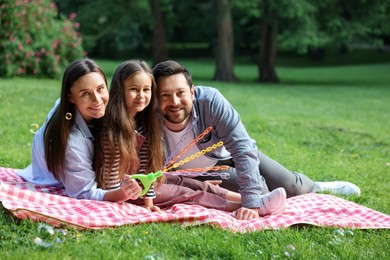 Photo of Happy family blowing soap bubbles on checkered picnic blanket in park