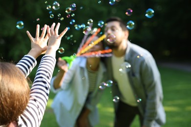 Photo of Family holiday getaway. Parents and daughter playing with soap bubbles outdoors, selective focus