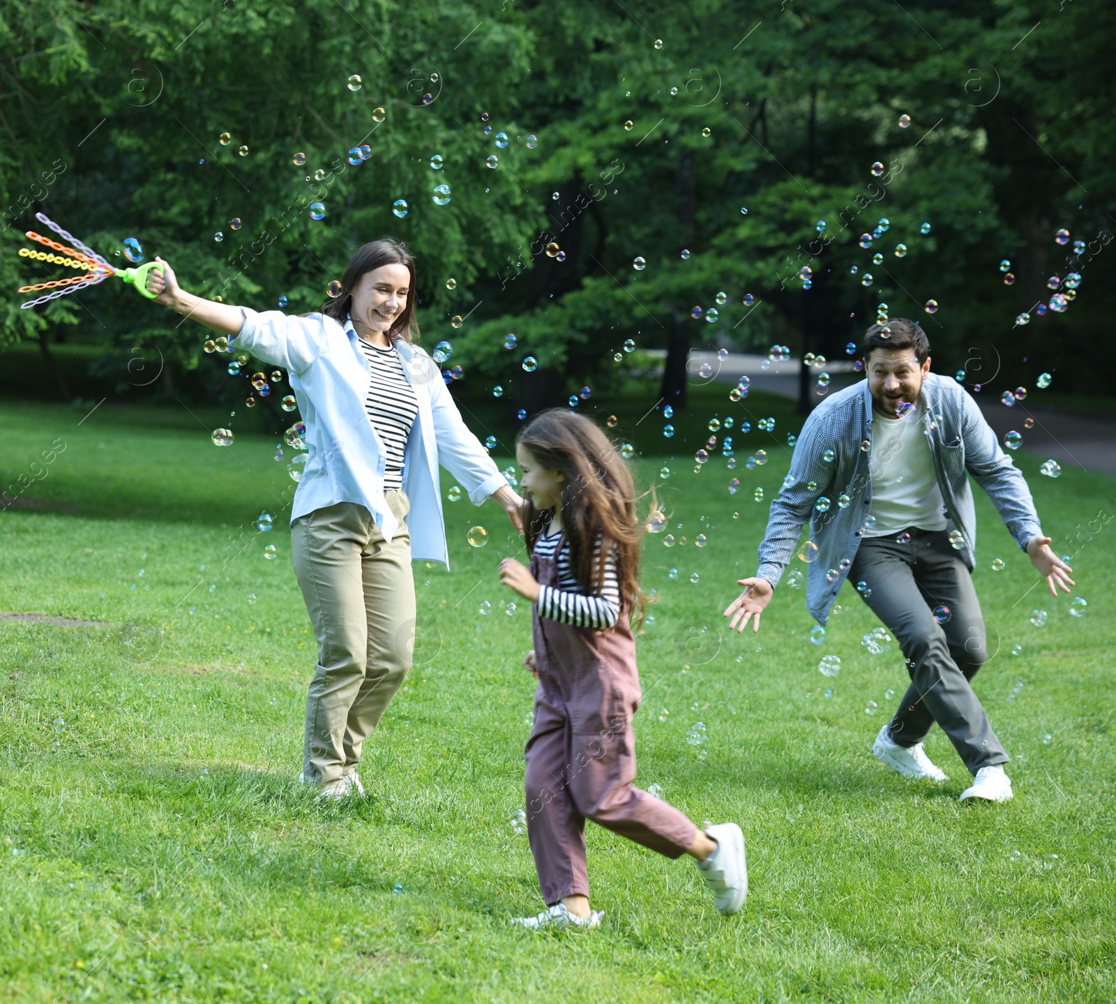 Family holiday getaway. Parents and daughter having fun with soap bubbles in park Photo of Family holiday getaway. Parents and daughter having fun with soap bubbles in park