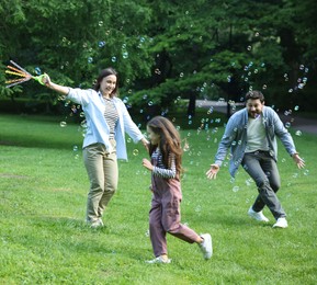 Photo of Family holiday getaway. Parents and daughter having fun with soap bubbles in park