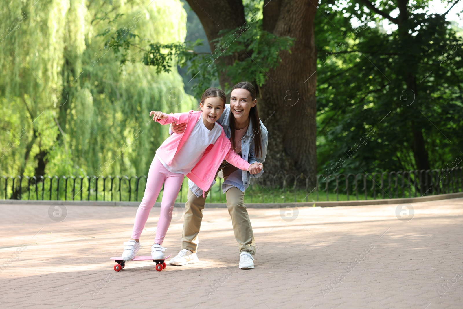 Photo of Family getaway. Happy mother and daughter having fun with penny board in park