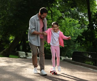 Photo of Family getaway. Happy father and daughter having fun with penny board in park