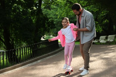 Photo of Family getaway. Happy father and daughter having fun with penny board in park. Space for text