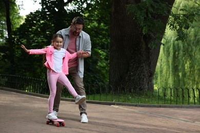 Photo of Family getaway. Happy father and daughter having fun with penny board in park. Space for text