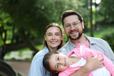 Photo of Family portrait of smiling parents and daughter outdoors