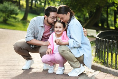 Photo of Family weekend. Parents kissing their happy daughter in park