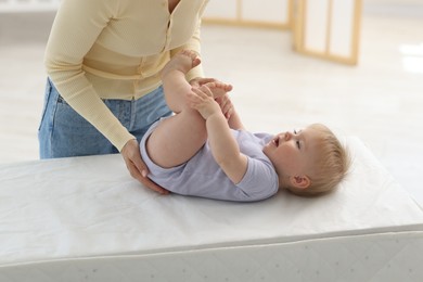 Photo of Mother playing with her cute baby on changing table at home, closeup