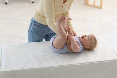 Photo of Mother playing with her cute baby on changing table at home, closeup