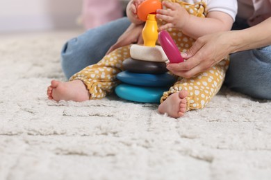 Photo of Mother and her little baby playing with toy pyramid on floor at home, closeup