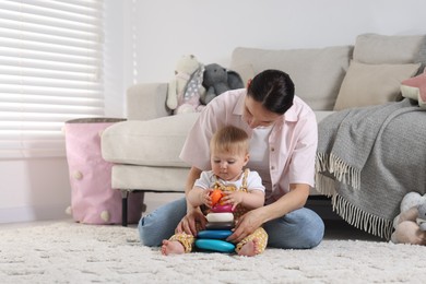 Photo of Mother and her little baby playing with toy pyramid on floor at home