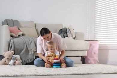 Photo of Mother and her little baby playing with toy pyramid on floor at home