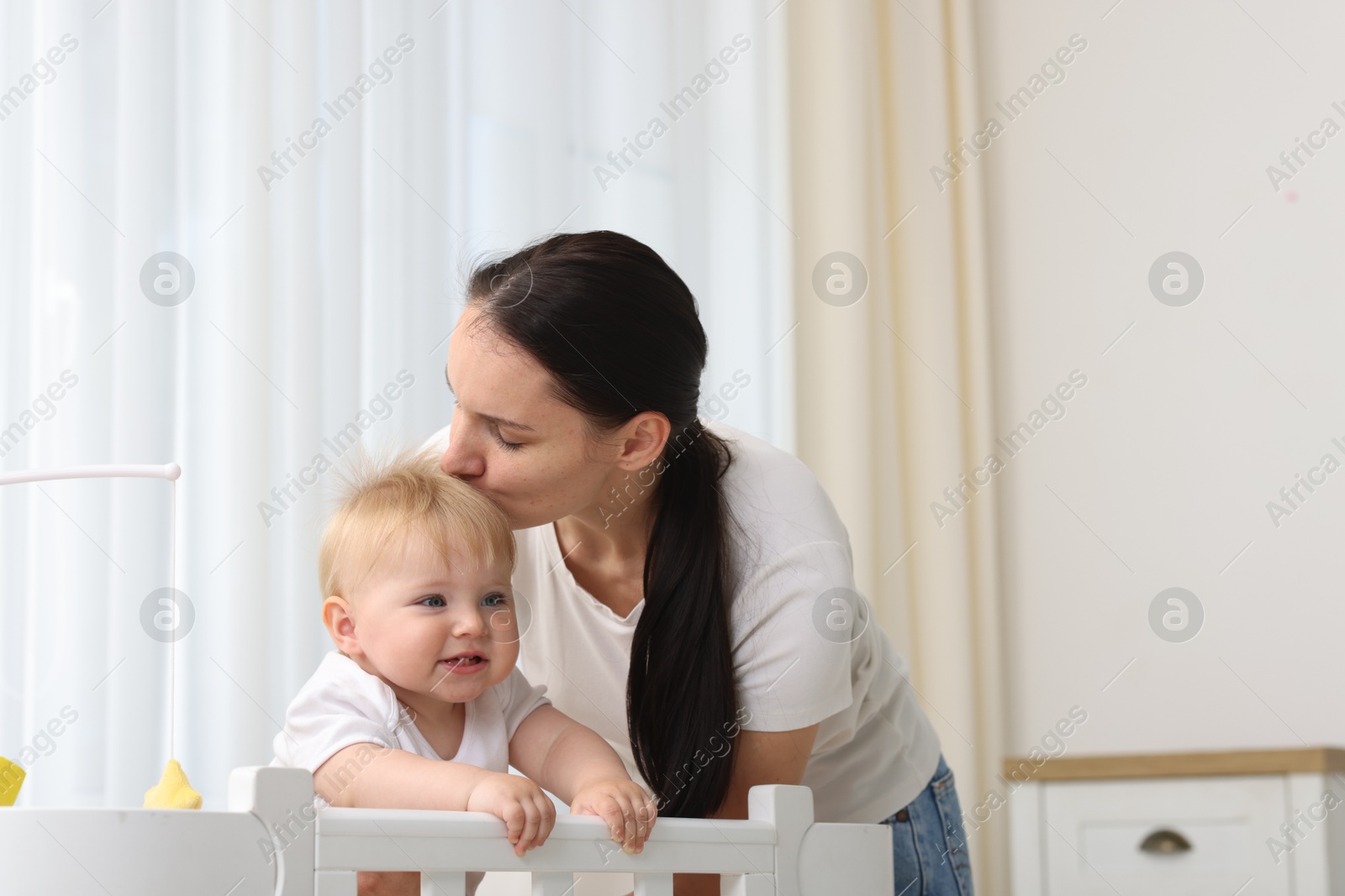 Photo of Mother kissing her cute baby in crib at home
