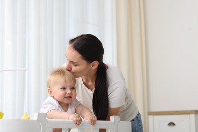 Photo of Mother kissing her cute baby in crib at home