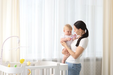 Photo of Mother with her little baby near crib at home