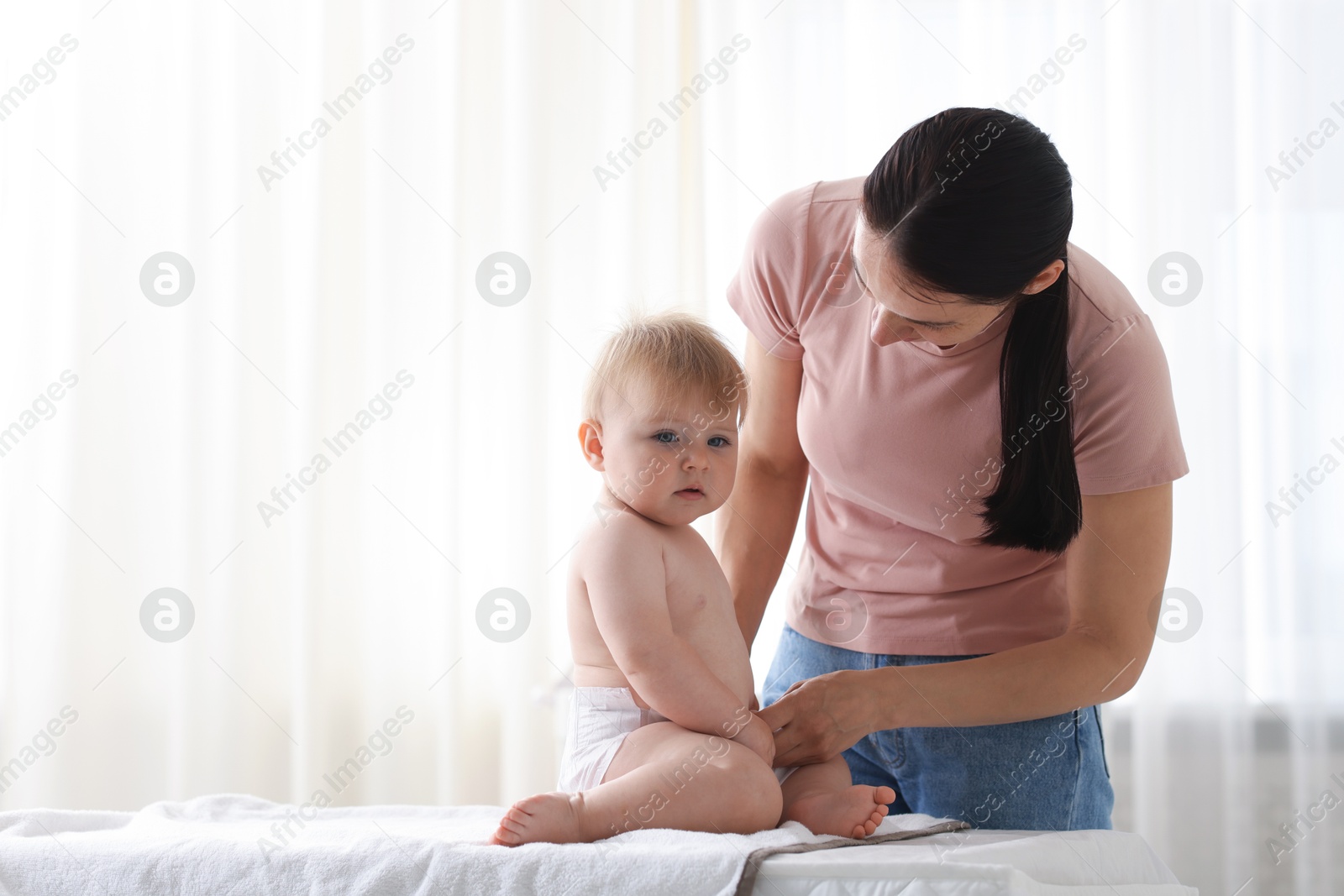 Mother changing her baby's diaper on table at home, space for text Photo of Mother changing her baby's diaper on table at home, space for text