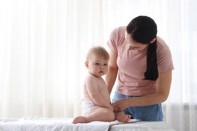 Photo of Mother changing her baby's diaper on table at home, space for text