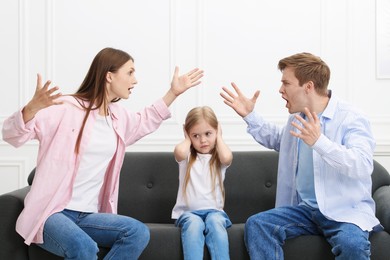 Photo of Upset little girl and her parents fighting on sofa at home
