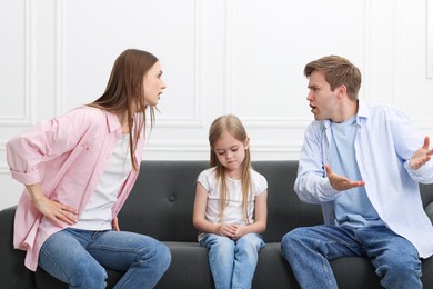 Photo of Upset little girl and her parents fighting on sofa at home