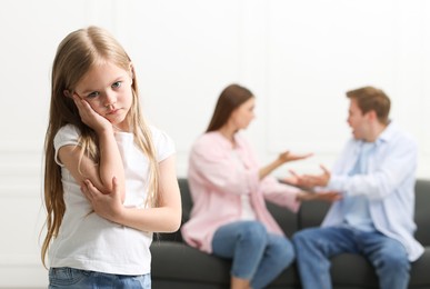 Photo of Upset little girl and her parents fighting at home, selective focus