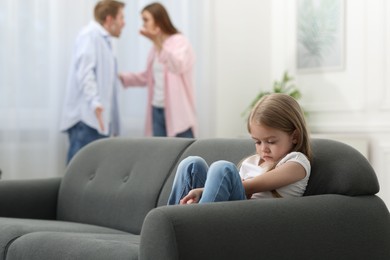 Photo of Upset little girl on sofa and her parents fighting at home, selective focus