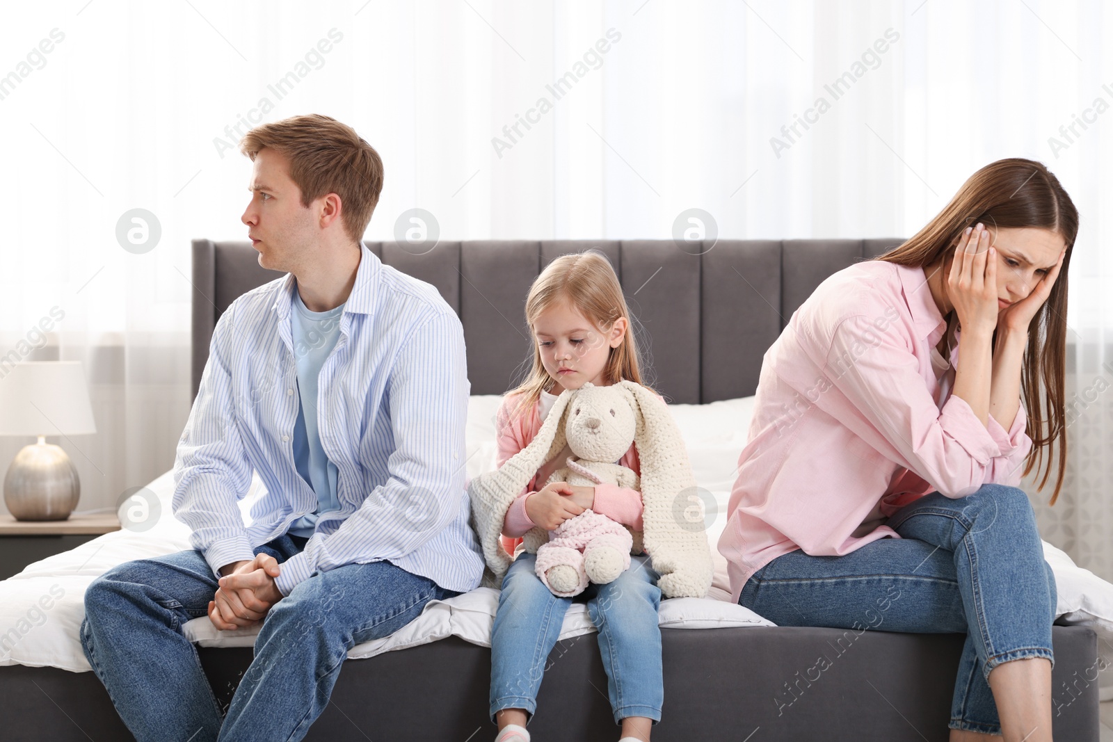 Upset little girl with bunny and her parents fighting on bed at home Photo of Upset little girl with bunny and her parents fighting on bed at home