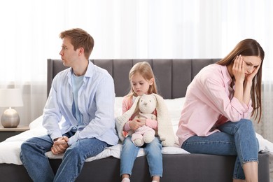 Photo of Upset little girl with bunny and her parents fighting on bed at home