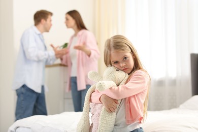 Photo of Upset little girl with bunny and her parents fighting at home, selective focus