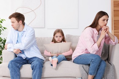 Photo of Upset little girl with pillow and her parents fighting on sofa at home