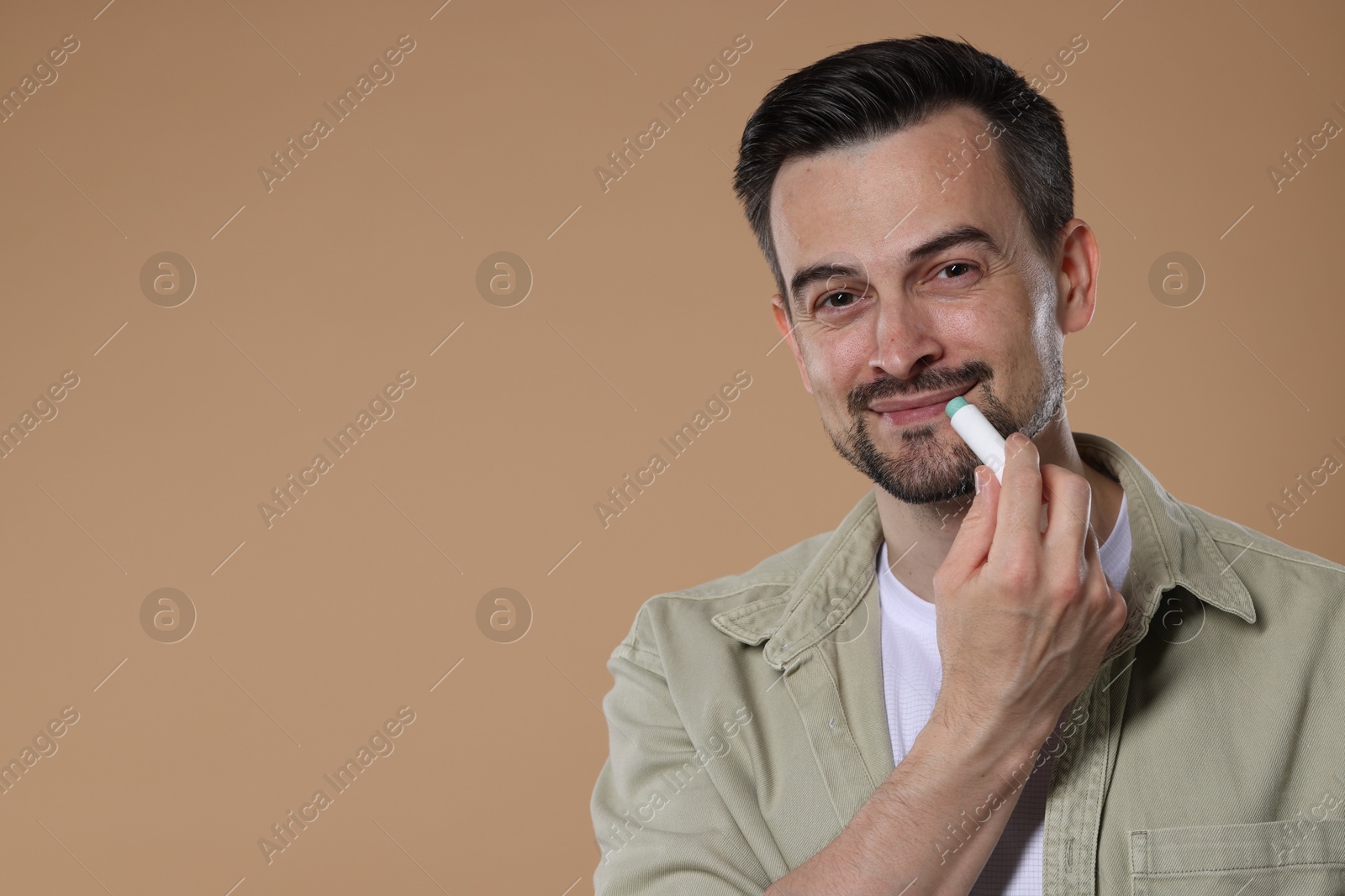 Handsome man applying lip balm onto his lips on light brown background. Space for text Photo of Handsome man applying lip balm onto his lips on light brown background. Space for text