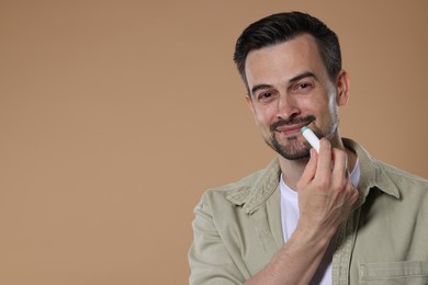 Photo of Handsome man applying lip balm onto his lips on light brown background. Space for text