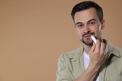 Photo of Handsome man applying lip balm onto his lips on light brown background. Space for text
