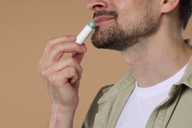 Photo of Man applying lip balm onto his lips on light brown background, closeup